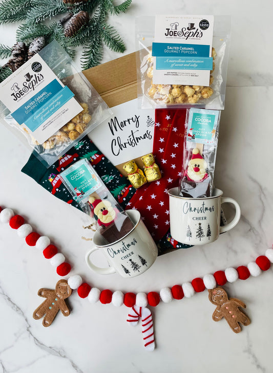 Couples movie night gift box containing, Christmas mugs, festive socks, santa hot chocolate spoons, slated caramel popcorn and Lindt gold bears. 