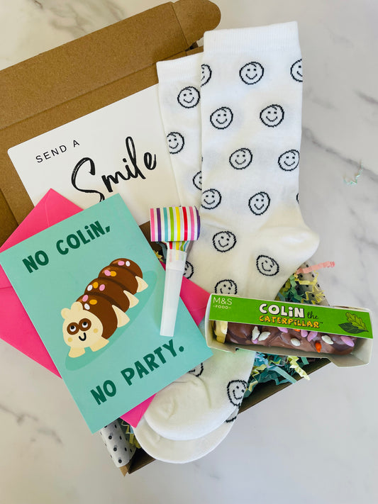  A vibrant Card displaying Colin the Caterpillar, No Colin, No Party, accompanied by a mini Colin the Caterpillar birthday cake, smiley face socks and birthday blower inside a birthday gift box.