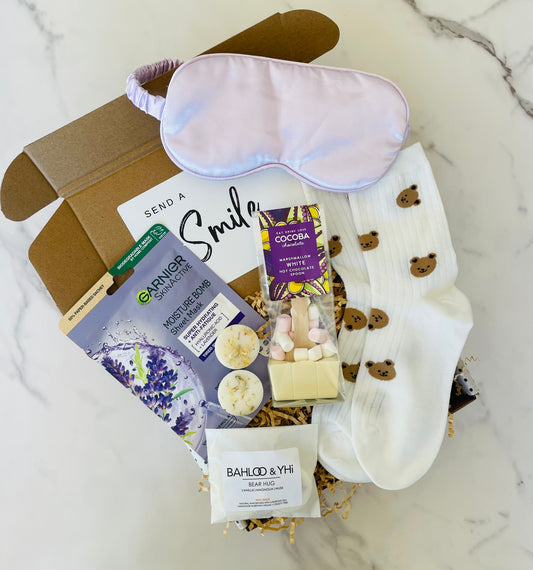 A delightful gift box containing a lilac sleep mask, face mask, bear socks, white chocolate hot chocolate spoon, bear hug wax melts. 