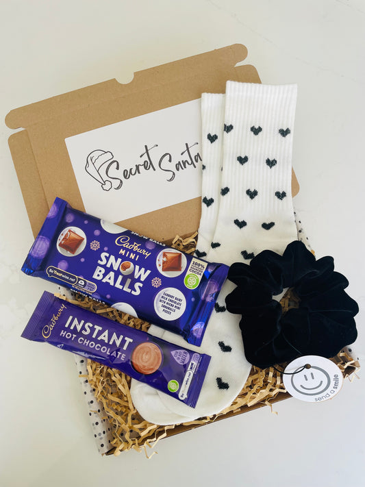 A Secret Santa Gift Box containing white socks with black hearts, a handmade black velvet scrunchie, Cadbury hot chocolate & Cadbury snow balls chocolate bar.  