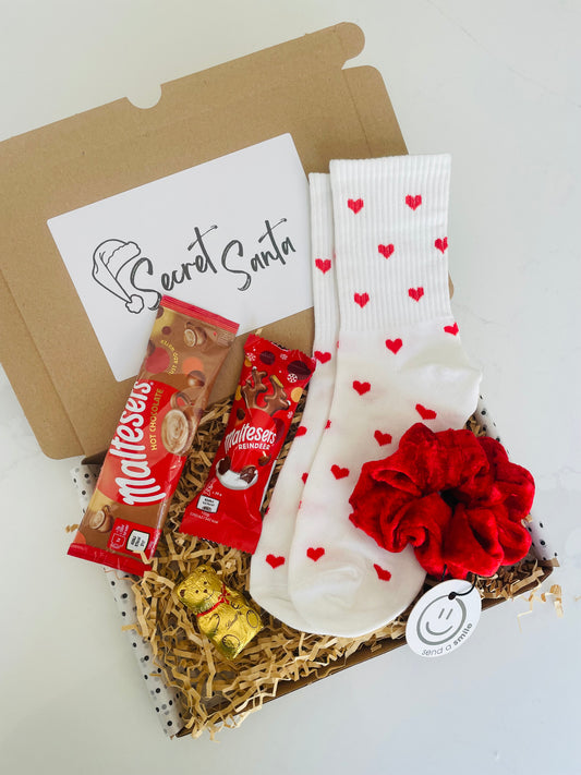 Secret Santa Gift Box containing Handmade red velvet scrunchie, white socks with red hearts, gold Lindt Bear, Maltesers Hot Chocolate and a Maltesers chocolate reindeer. 