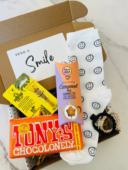 A gift box featuring smiley socks, Caramel Tea, Tony's Chocolonely salted caramel chocolate, hair ties & paw paw lip balm. 